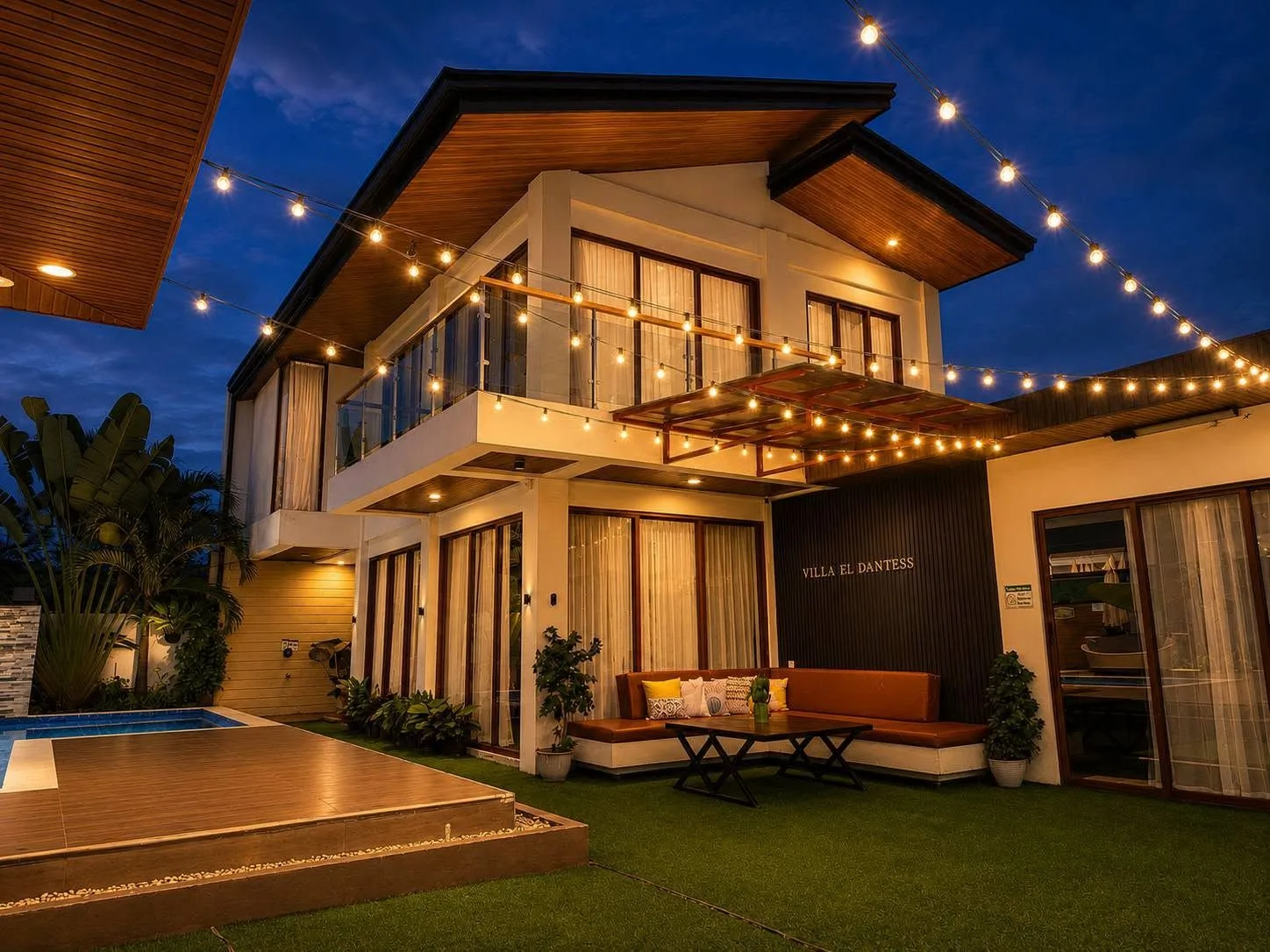 Villa El Dantess at blue hour: the two-storey villa lit up under festoon string lights, the lounge and the pool deck on the lawn